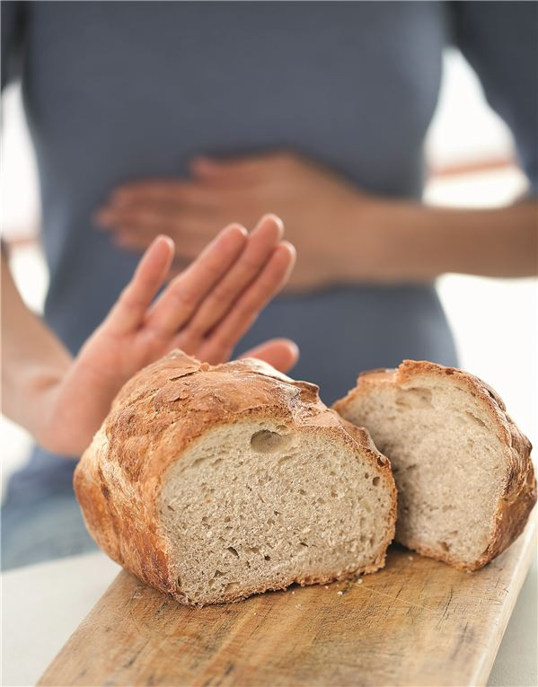 Brot im Vordergrund, Frau im Hintergrund hält sich den Magen.