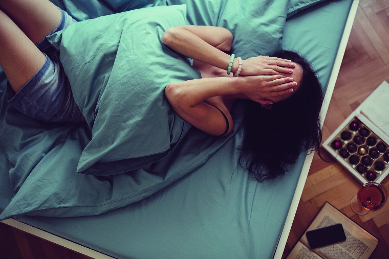 Frau im Bett hält sich vor Schmerzen die Hände vors Gesicht.