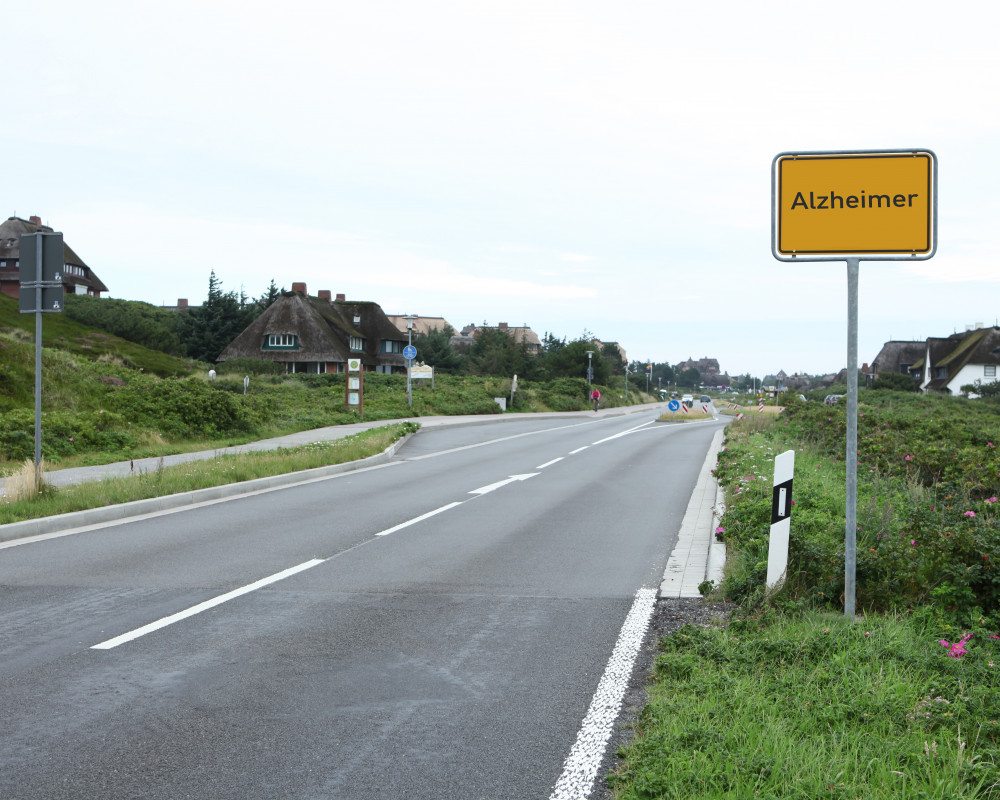 Leere Straße mit Ortsschild auf dem Alzheimer steht