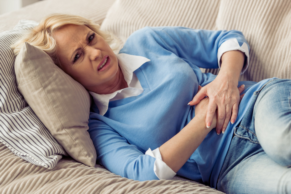 Unter Magen-Darm-Krämpfen leidende Frau liegt auf der Couch