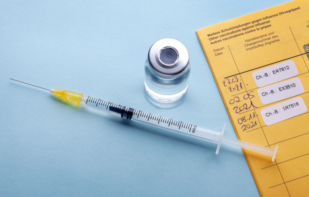Gelber Impfausweis mit drei Chargen-Etiketten und darüber liegender Spritze