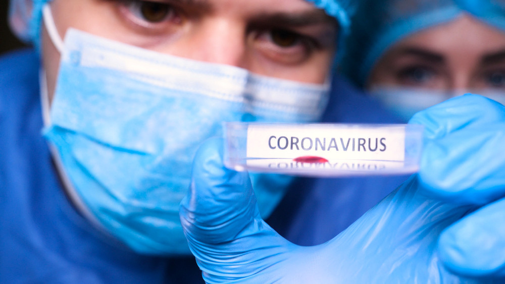 Mann mit Mundschutz hält Teströhrchen mit Aufschrift Coronavirus