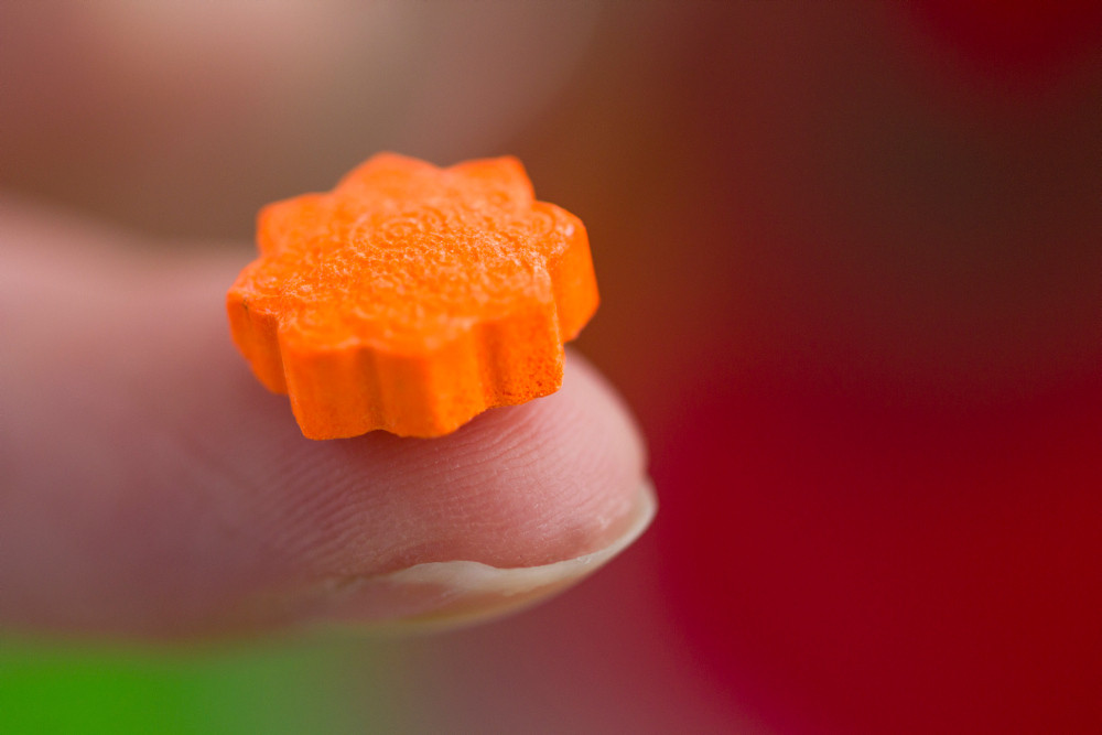 Orangefarbene Ecstasy Tablette in Großaufnahme auf einem Zeigefinger gehalten