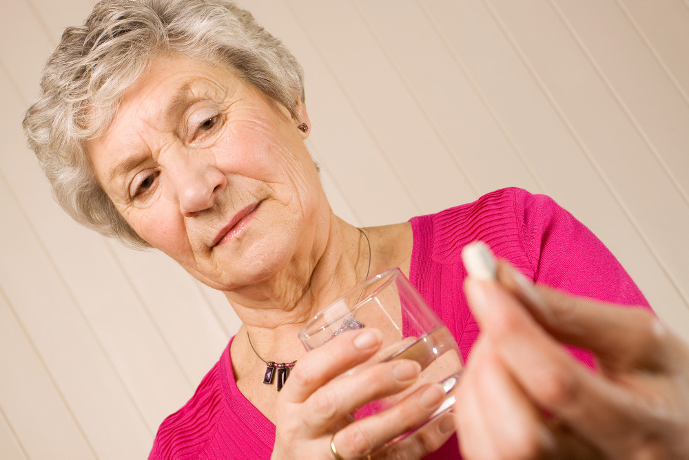 Frau mit einem Glas Wasser in der Hand blickt skeptisch auf eine Tablette