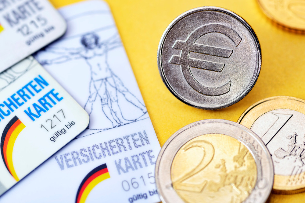 Versichertenkarten neben Euromünzen Versichertenkarten neben Euromünzen