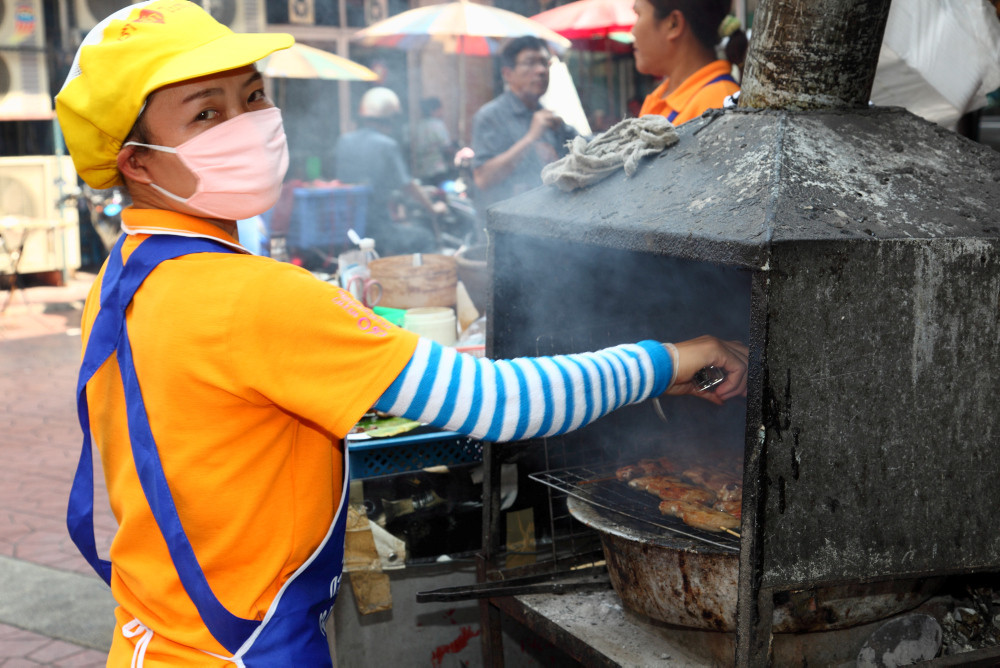 Chinesische Frau mit Atemmaske am Grill Chinesische Frau mit Atemmaske am Grill