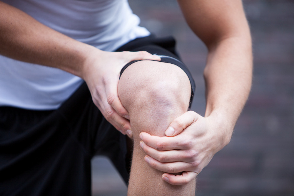 Ein junger Mann in Sportbekleidung fasst sich an sein Knie. Ein junger Mann in Sportbekleidung fasst sich an sein Knie.