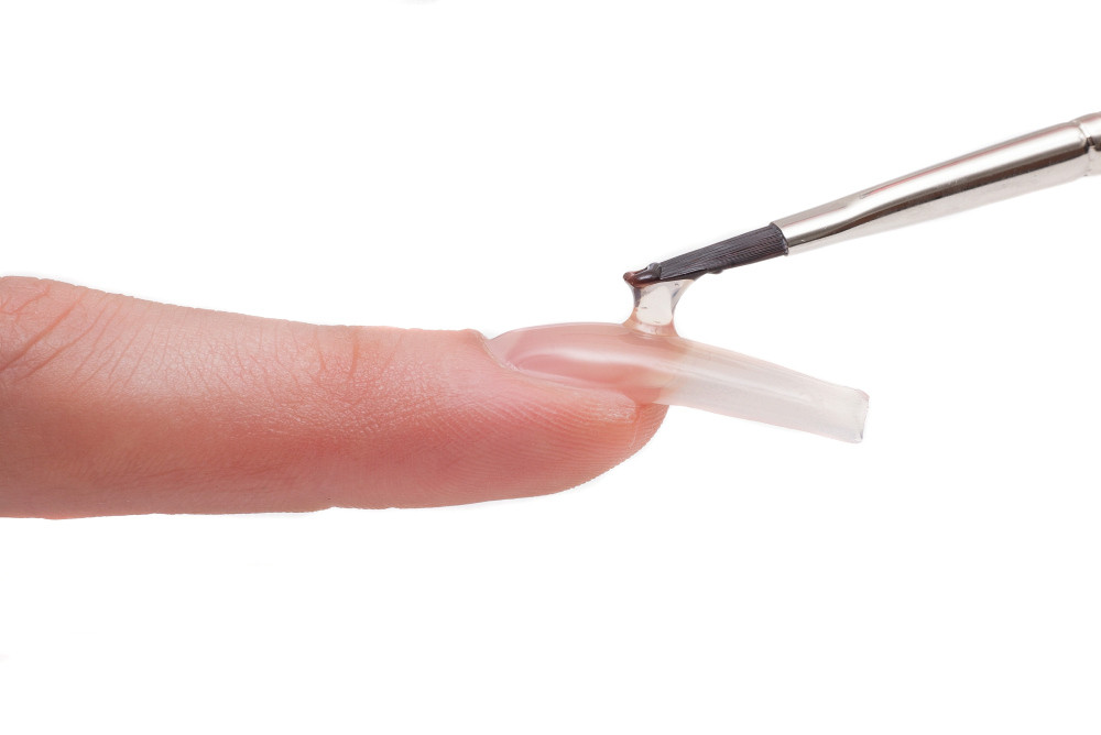 Ein künstlicher Fingernagel wird mit Gel bepinselt. Ein künstlicher Fingernagel wird mit Gel bepinselt.