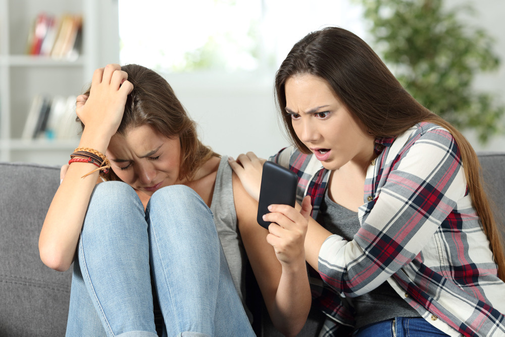 Trauiges Mädchen zeigt ihrer Freundin ein Smartphone mit schlechten Neuigkeiten Trauiges Mädchen zeigt ihrer Freundin ein Smartphone mit schlechten Neuigkeiten