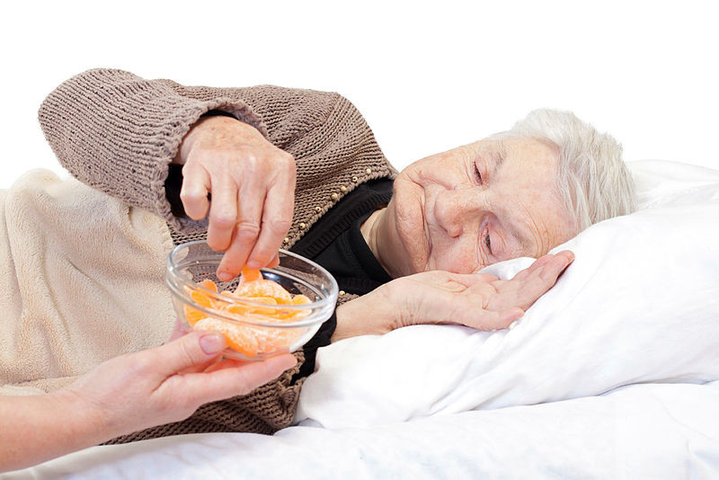 Bettlägerige Seniorin nimmt sich ein Stück Mandarine aus einem gereichten Schälchen