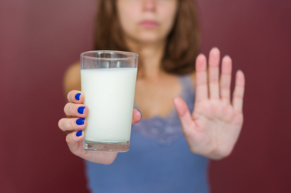 Frau hält Glas Milch gestreckt nach vorne und symbolisiert mit dem anderen Arm „Stopp“

