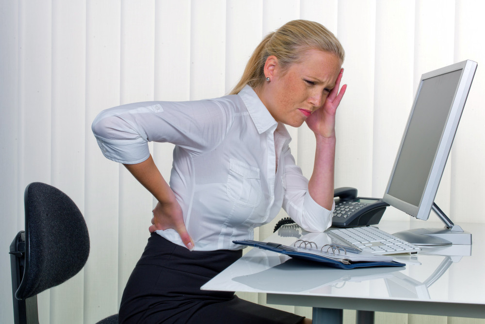 Frau mit Rückenschmerzen sitzt vor dem Computer