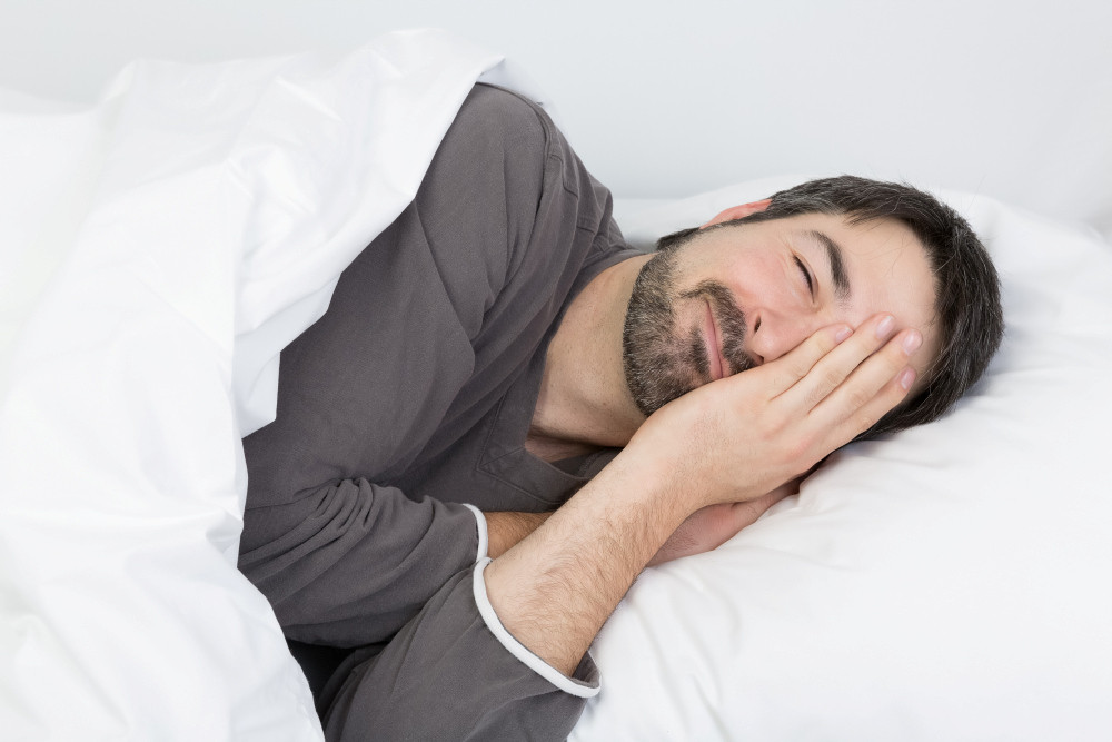 Mann liegt im Bett und hält sich mit der Hand das linke Auge zu
