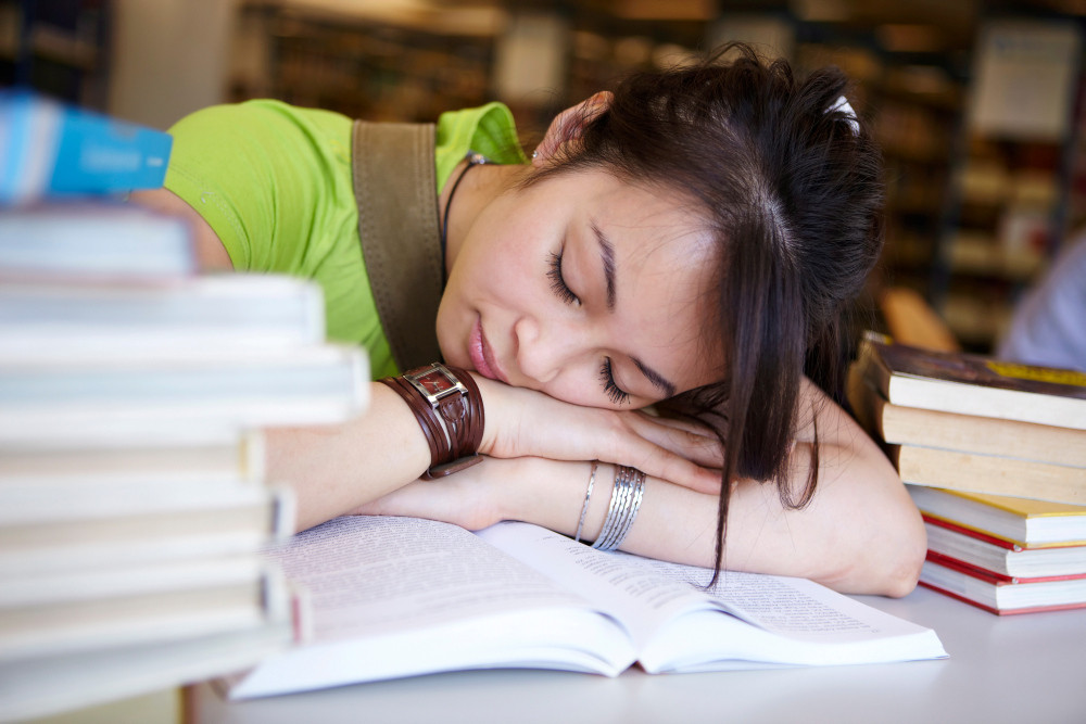 Schülerin schläft über einem Buch ein