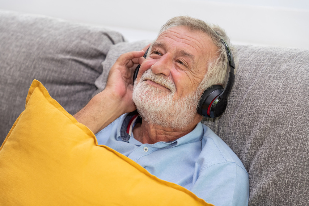 Älterer Mann hört mit Kopfhörern auf dem Sofa Musik