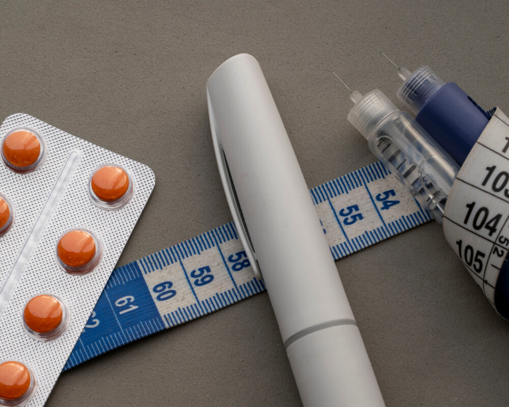 Tablettenblister, Pens und ein Maßband als Symbolbild für Medikamente zur Gewichtsreduktion.