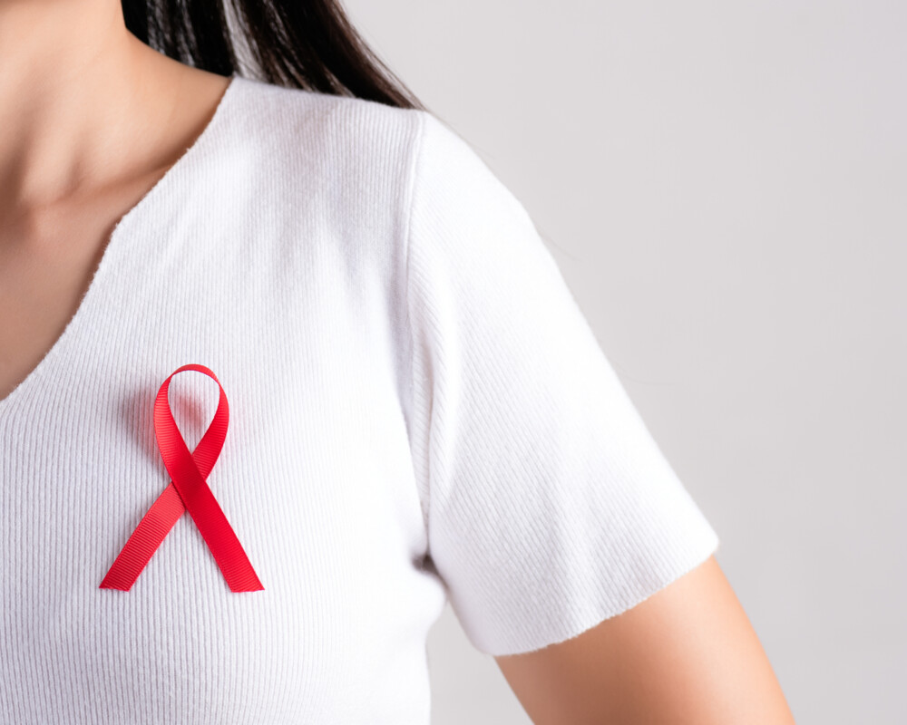Frau im weißen T-Shirt im Anschnitt mit roter Schleife als Symbol für die Solidarität mit Menschen, die von HIV und Aids betroffen sind.