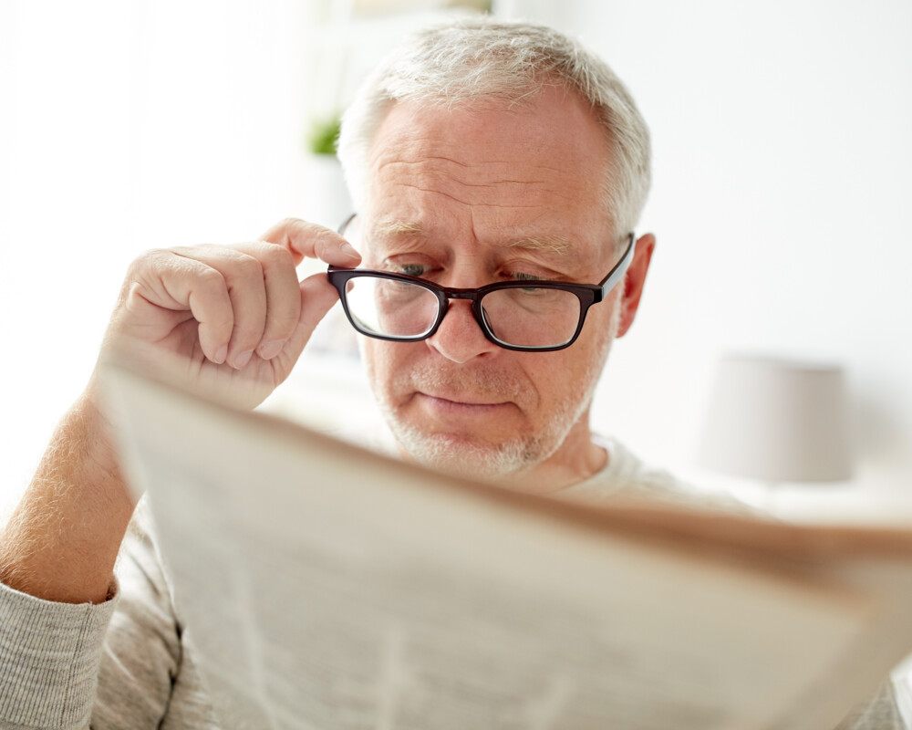 Senior mit grauem Haar und schwarzer Brille liest Zeitung