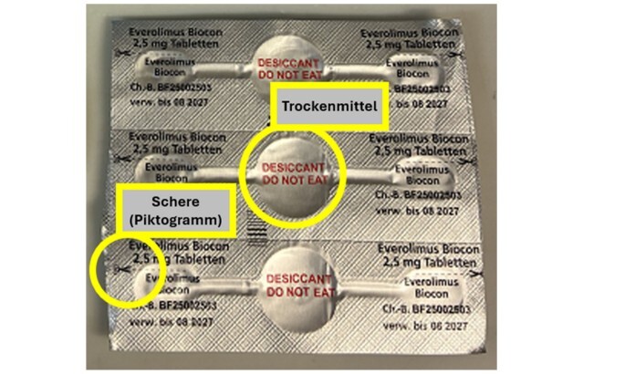 Zerschnittener Blister mit Blisternäpfen für wirkstoffhaltige Tabletten und dem mittig positionierten Trockenmittel mit der Aufschrift "DESICCANT, DO NOT EAT", Zusätzlich Piktogramm einer Schere mit vorgezeichneter Perforationslinie.