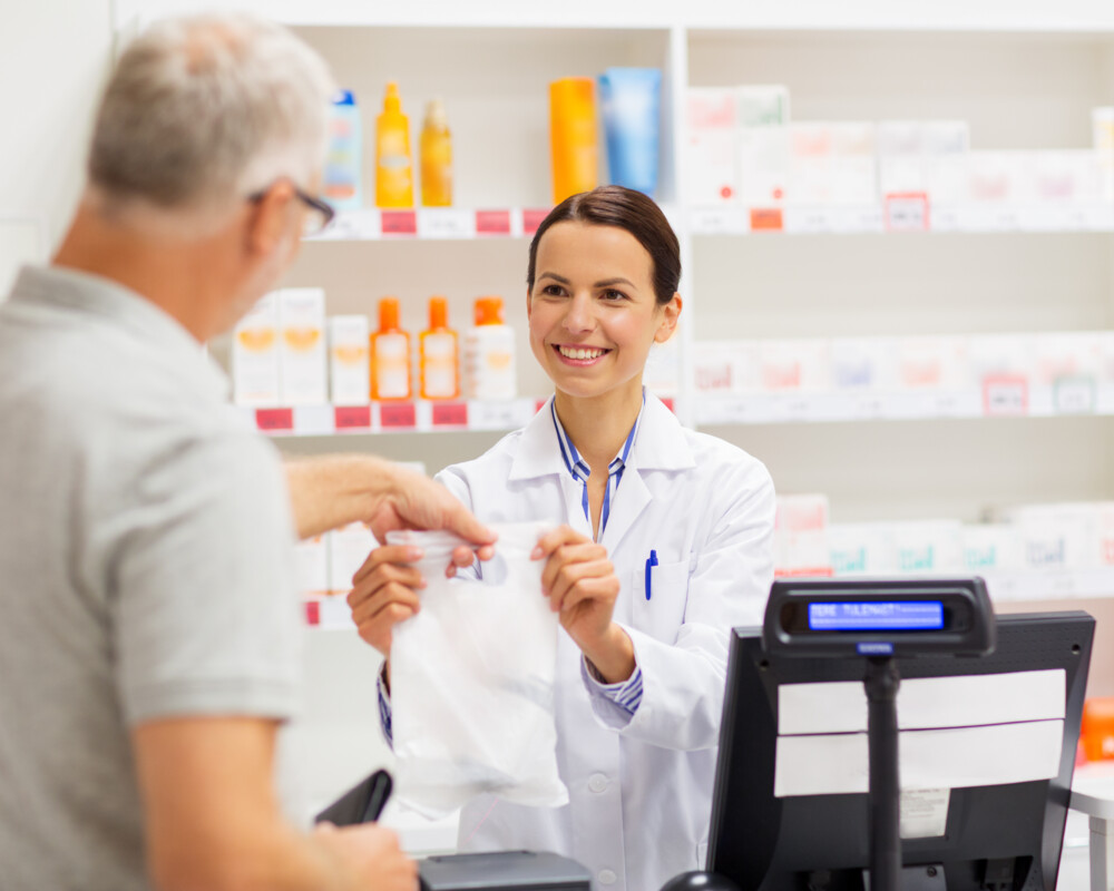 PTA/Apothekerin reicht einem Kunden eine Tüte mit Arzneimitteln.