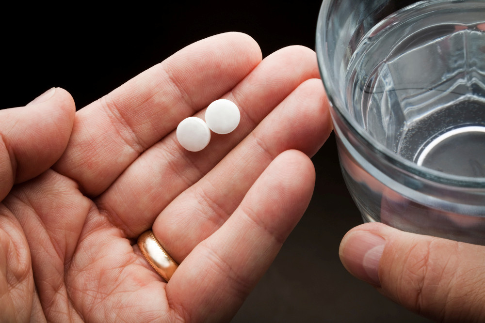 Linke Hand hält zwei Tabletten, rechte ein Wasserglas