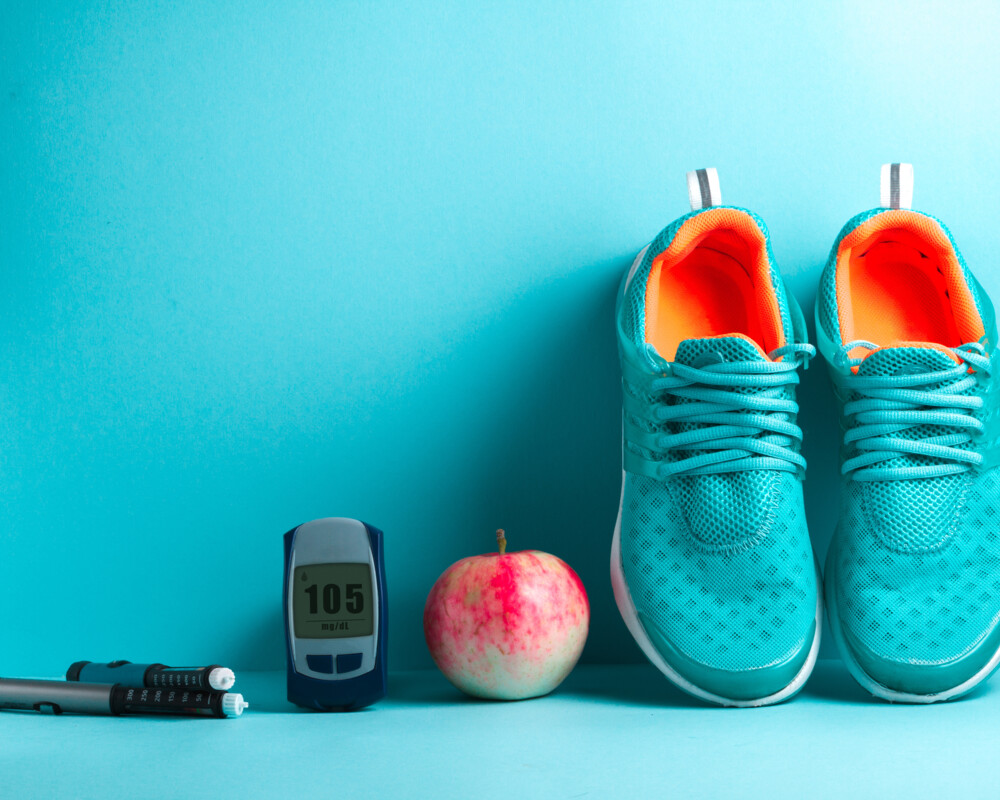 Insulin-Pens, Glukosemessgerät, Apfel, Sportschuhe in Reihe vor türkisfarbenem Hintergrund