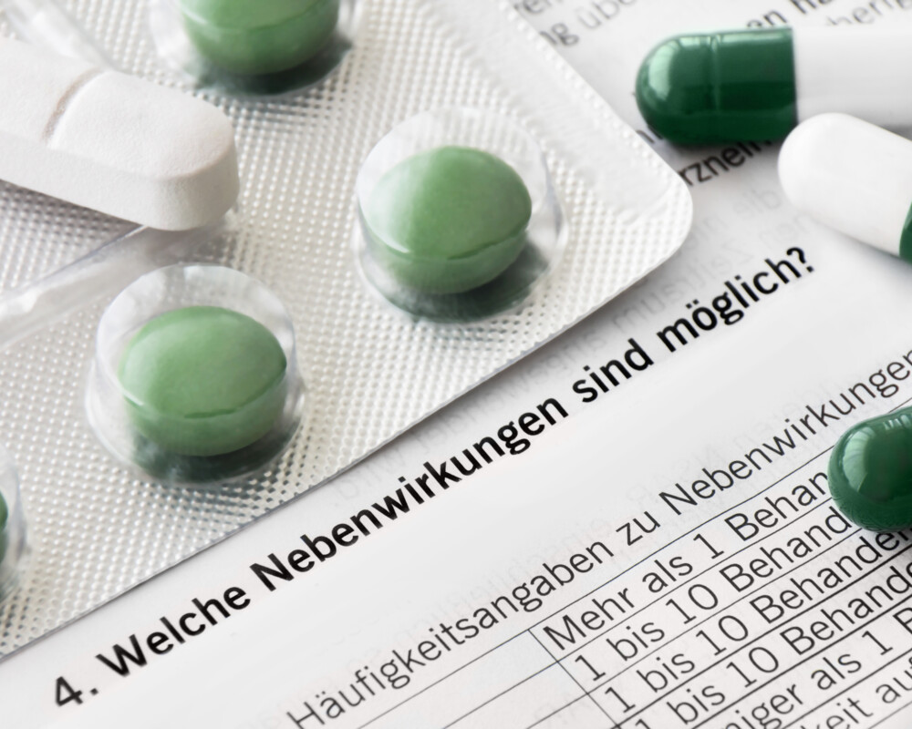 Grüne Tabletten im Blister, grün-weiße Kapseln und weiße, teilbare Tabletten auf einem Beipackzettel liegend.