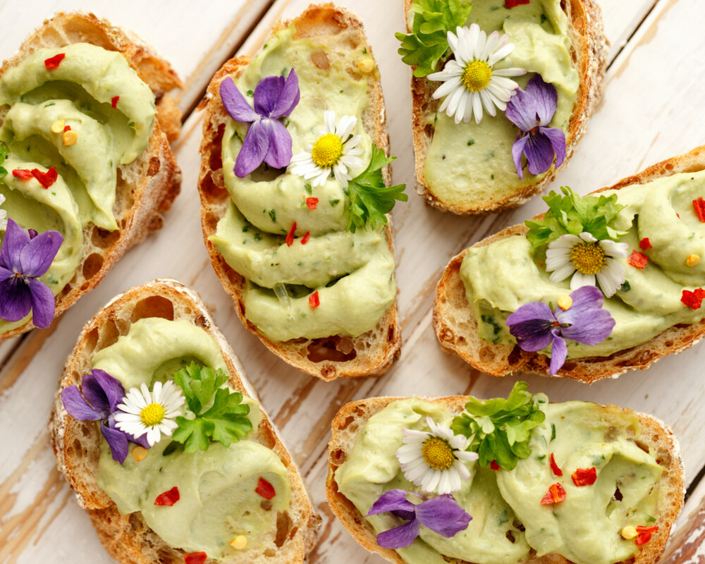 Kanapees mit Avocadopaste und essbaren Blüten auf Holzhintergrund