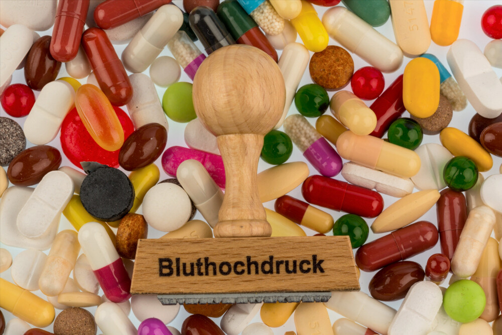 Stempel mit Aufschrift „Bluthochdruck“ auf verschiedenen bunten Tabletten und Kapseln