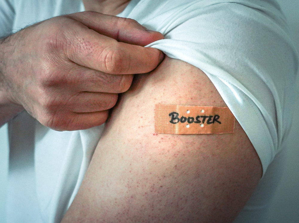Impfarm mit Pflaster beschriftet mit „Booster“