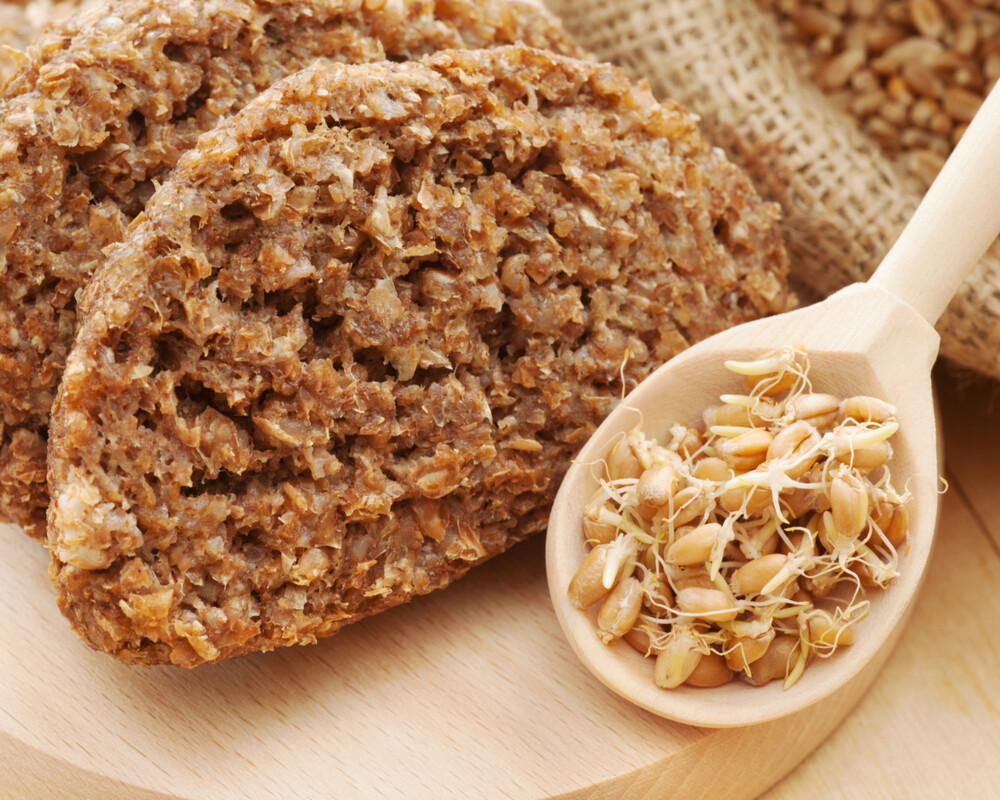 Brot aus Weizensprossen und gekeimten Samen in Löffeln auf Schneidebrett