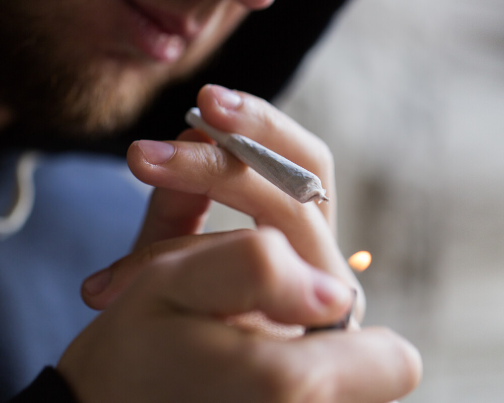 Nahaufnahme eines jungen Mannes, der sich einen Joint anzündet.