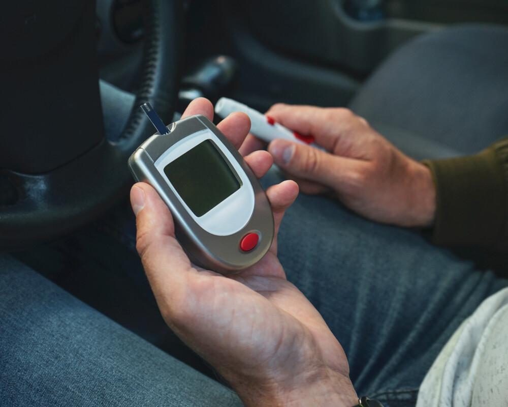 Mann sitzt im Autor auf der Fahrerseite und hält Glukosemessgerät in der Hand