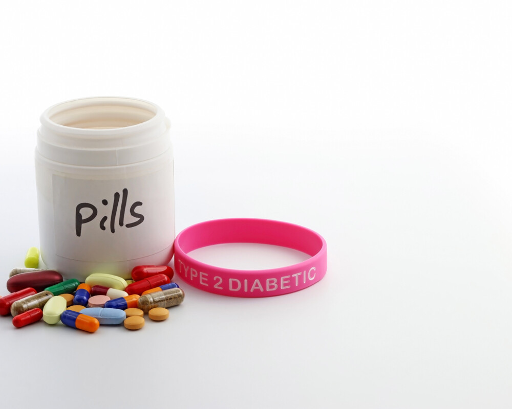 Medikamentendose mit Aufschrift „Pills“, davor Kapseln und Tabletten sowie ein rosafarbenes Armband mit Aufschrift Type 2 Diabetic