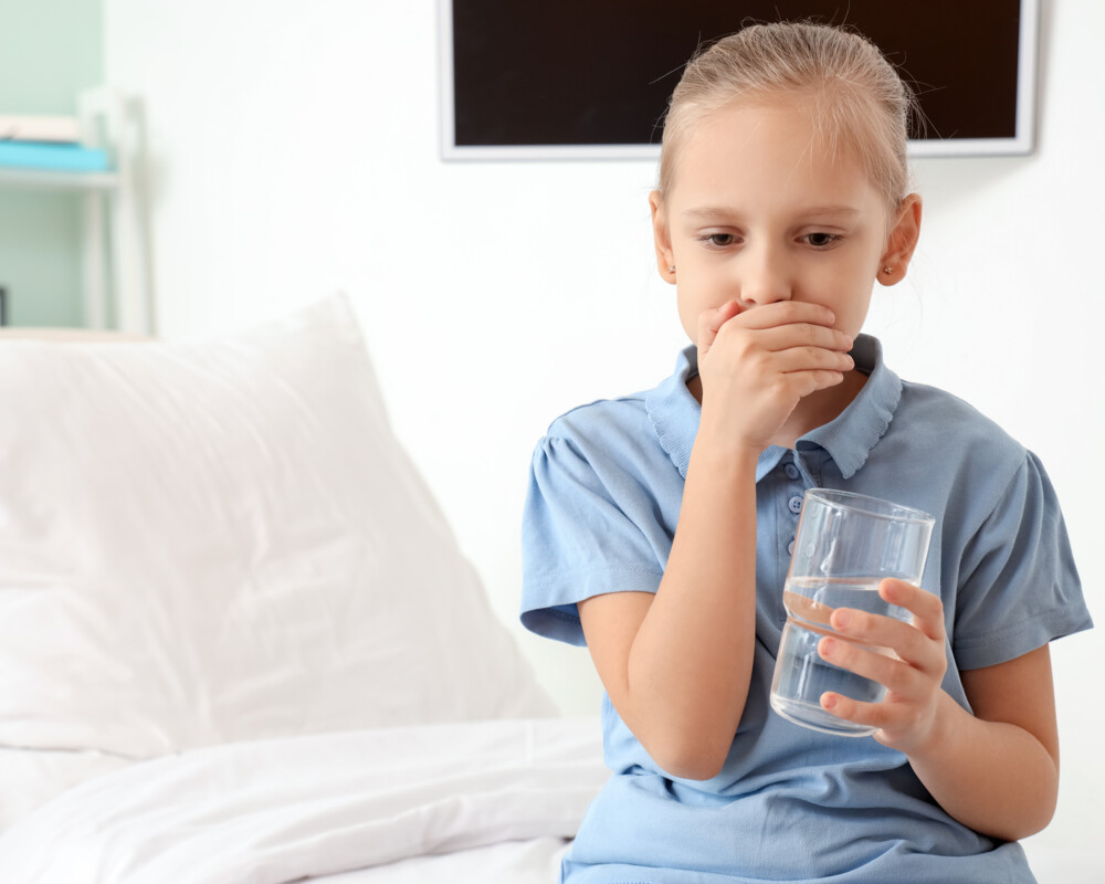 Mädchen sitzt auf Bettkante mit einem Glas Wasser in der einen Hand, die andere Hand hält sie vor den Mund. Mädchen sitzt auf Bettkante mit einem Glas Wasser in der einen Hand, die andere Hand hält sie vor den Mund.