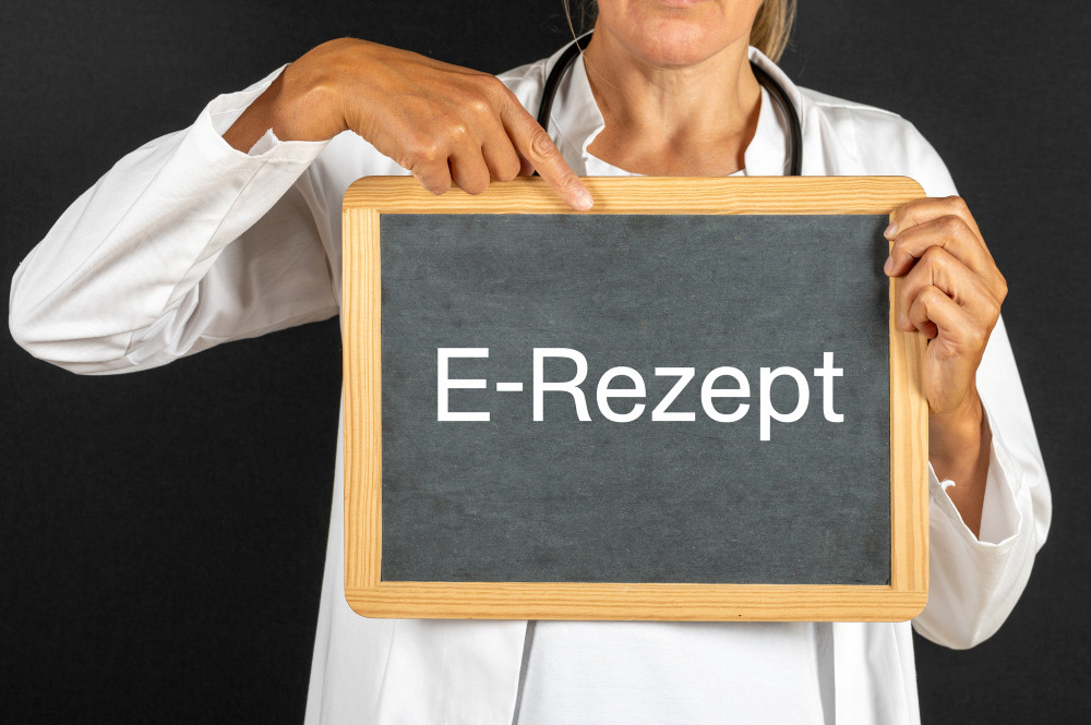 Frau im weißen Kittel hält Kreidetafel mit Aufschrift E-Rezept in den Händen