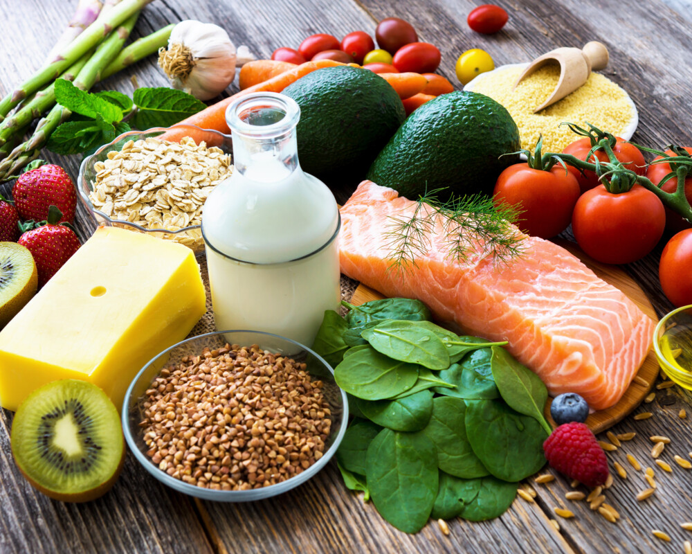 Symbolbild für eine gesunde Kost: Käse, Milch, Lachs, Tomaten, Spargel, Haferflocken, Karotten, Spinat und Früchte wie Kiwi, Himbeere, Erdbeere und andere Lebensmittel.