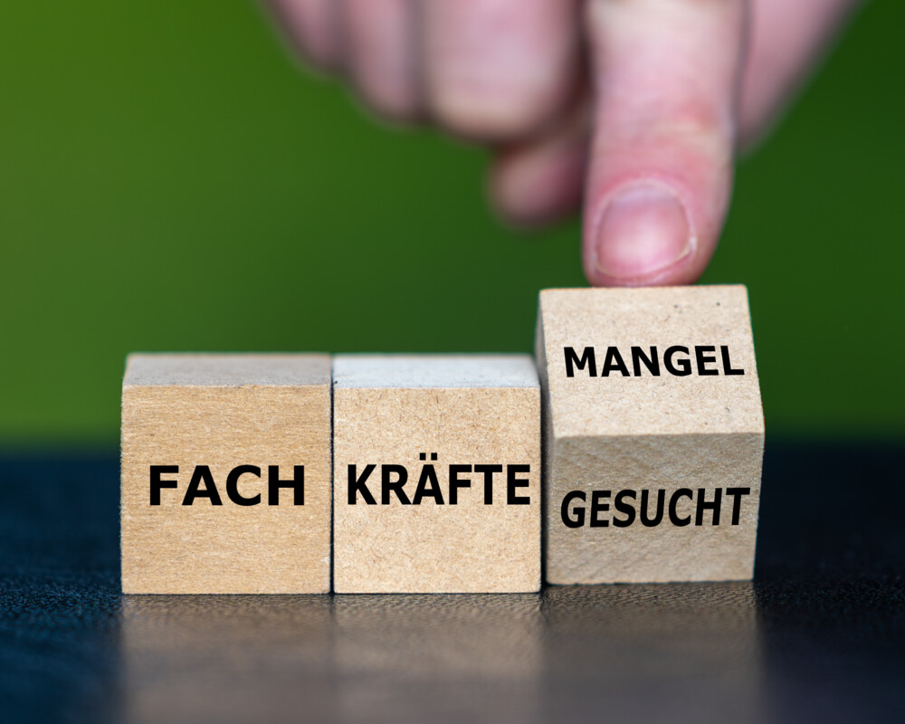 Hand dreht Würfel und ändert den Ausdruck „Fachkräfte gesucht“ in „Fachkräftemangel“.
