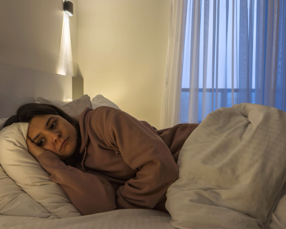 Junge Frau antriebslos und traurig im Bett liegend.
