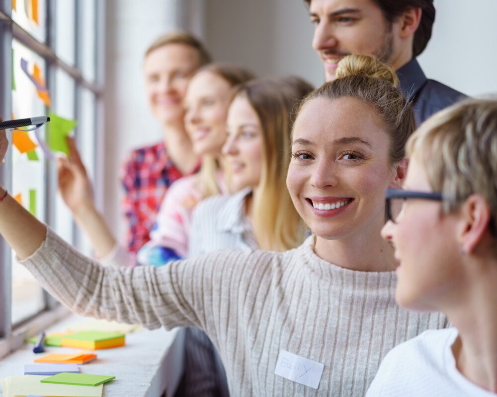 Gruppenarbeit mit Post-its – Notizzettel werden am Fenster angeklebt