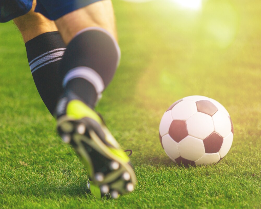 Fußballer auf dem Rasen in Begriff den Ball zu schießen; Ausschnitt Waden