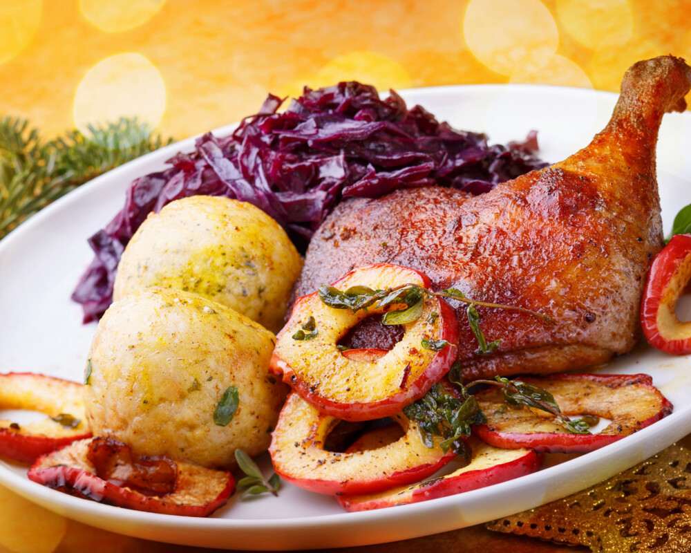 Gänsekeule mit Rotkohl, Klößen und Apfelringen auf einem Teller arrangiert.