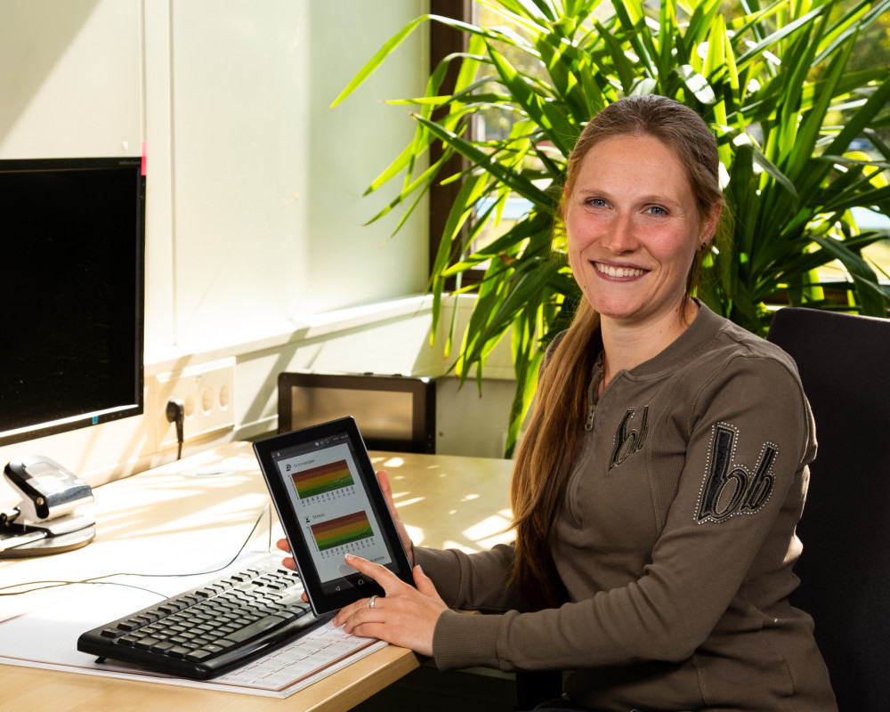 Dr. Corinna Faust-Christmann sitzt am Schreibtisch und zeigt die Stress-App auf dem Tablet.