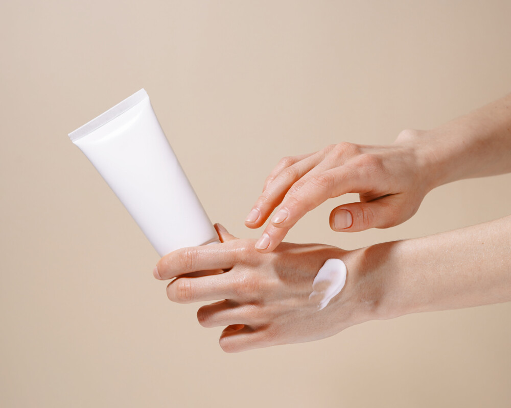 Linke Hand hält Handcreme, rechte cremt Hand ein.