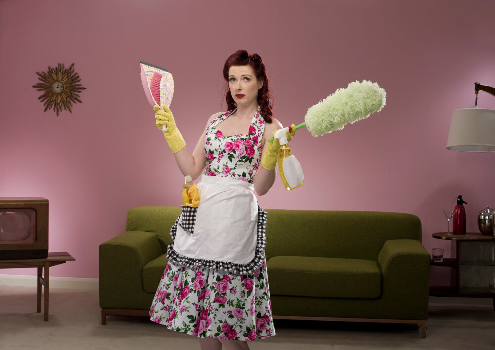 Hausfrau im Retrolook mit Schürze und Kleid, Staubwedel und Handfeger und Schaufel in der Hand. Hausfrau im Retrolook mit Schürze und Kleid, Staubwedel und Handfeger und Schaufel in der Hand.