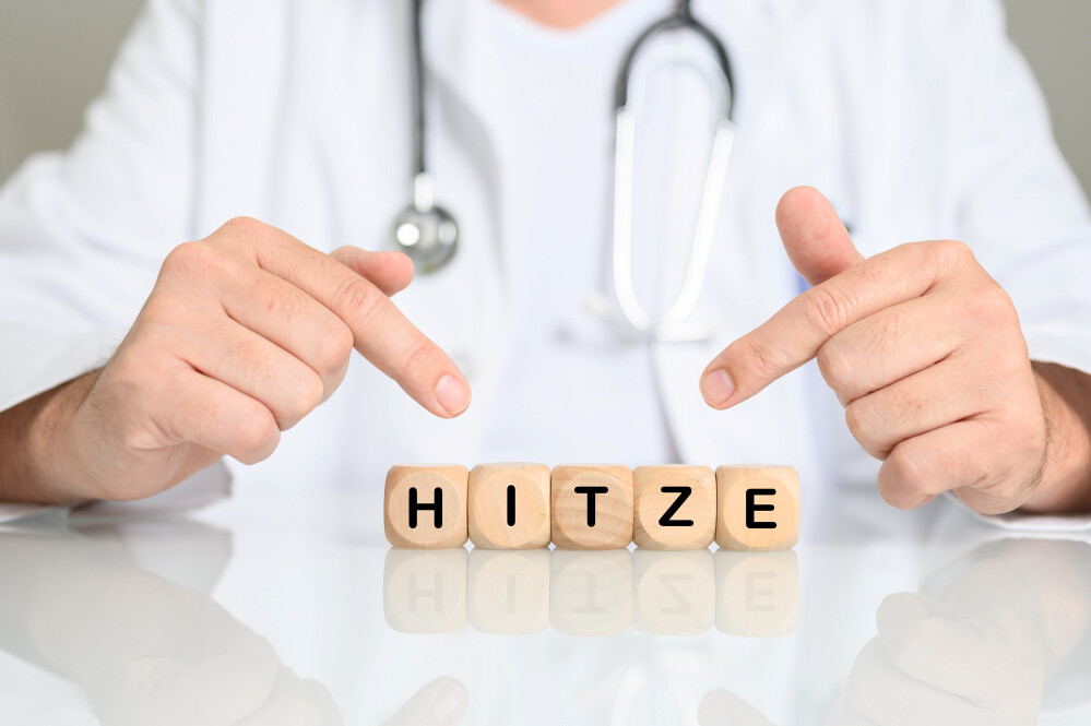 Mann mit Stethoskop um den Hals zeigt auf Holzwürfel, die das Wort HITZE bilden Mann mit Stethoskop um den Hals zeigt auf Holzwürfel, die das Wort HITZE bilden