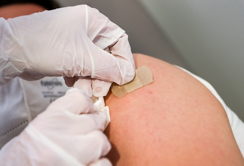 Geimpfter Person wird ein Pflaster auf die Impfstelle am Arm geklebt.