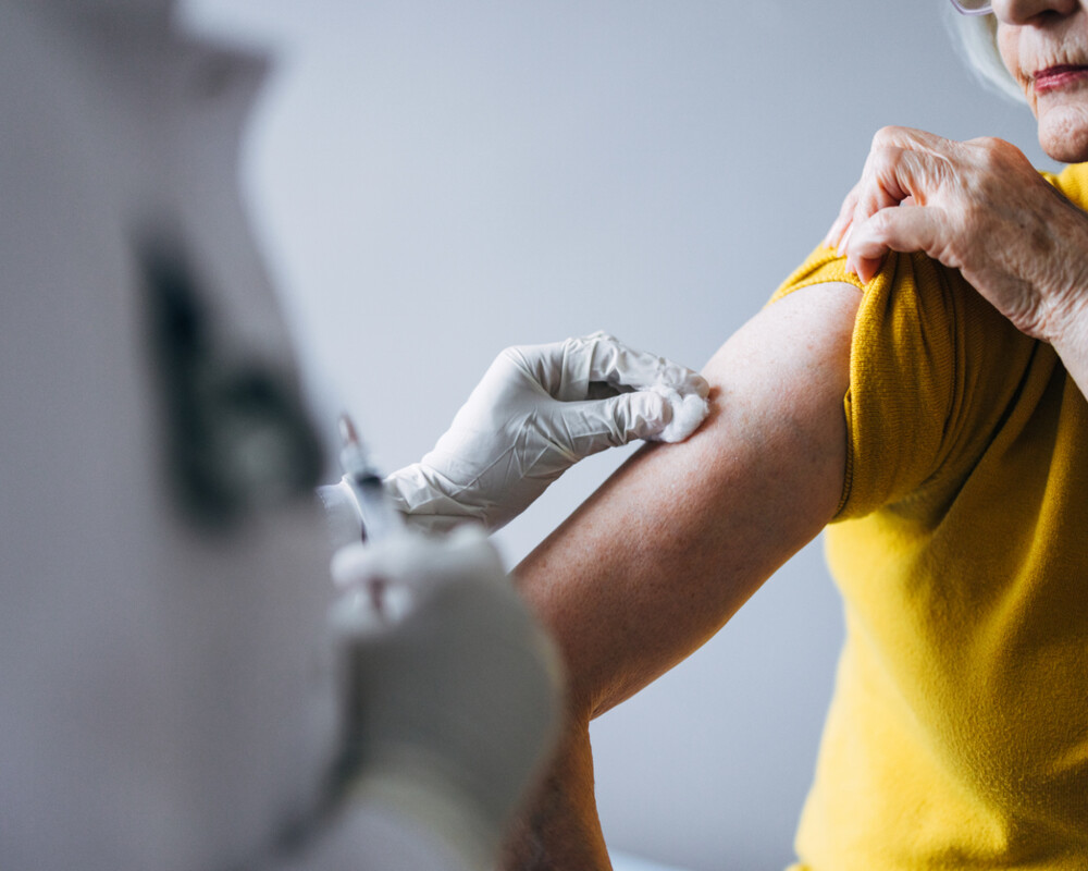 Seniorin, die von medizinischem Fachpersonal in Schutzhandschuhen geimpft wird
