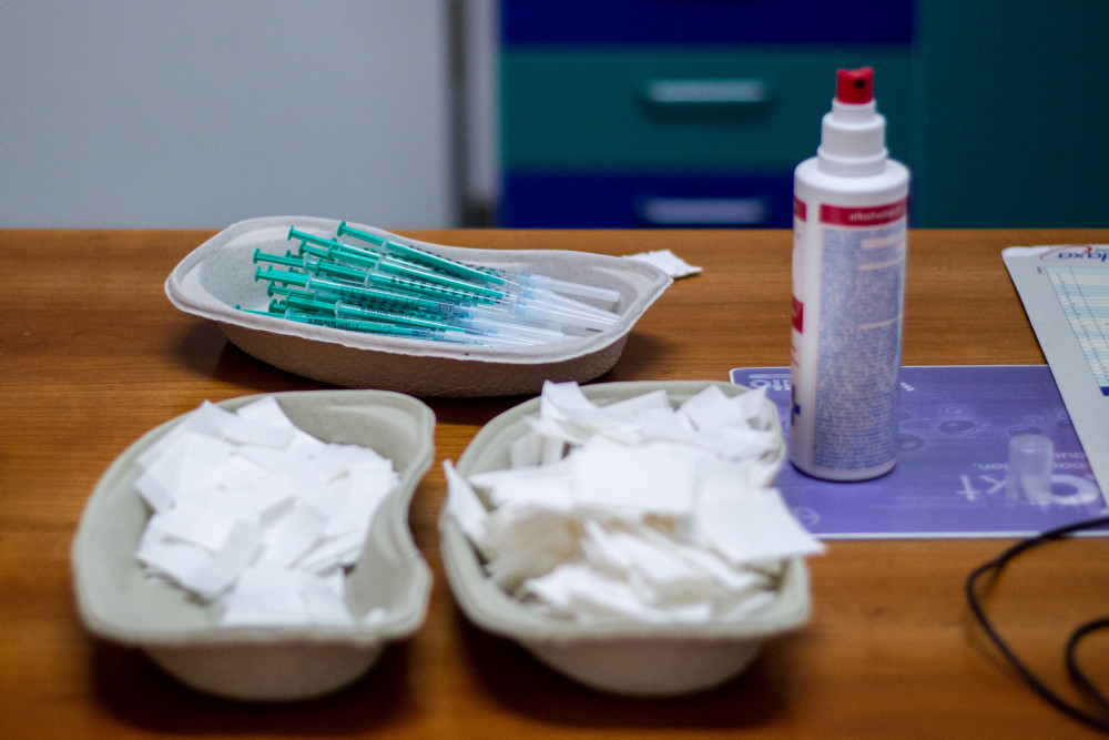 Aufgezogene Spritze mit Impfstoff in einer Pappschale, davor Mulltupfer und eine Flasche Desinfektionsmittel
