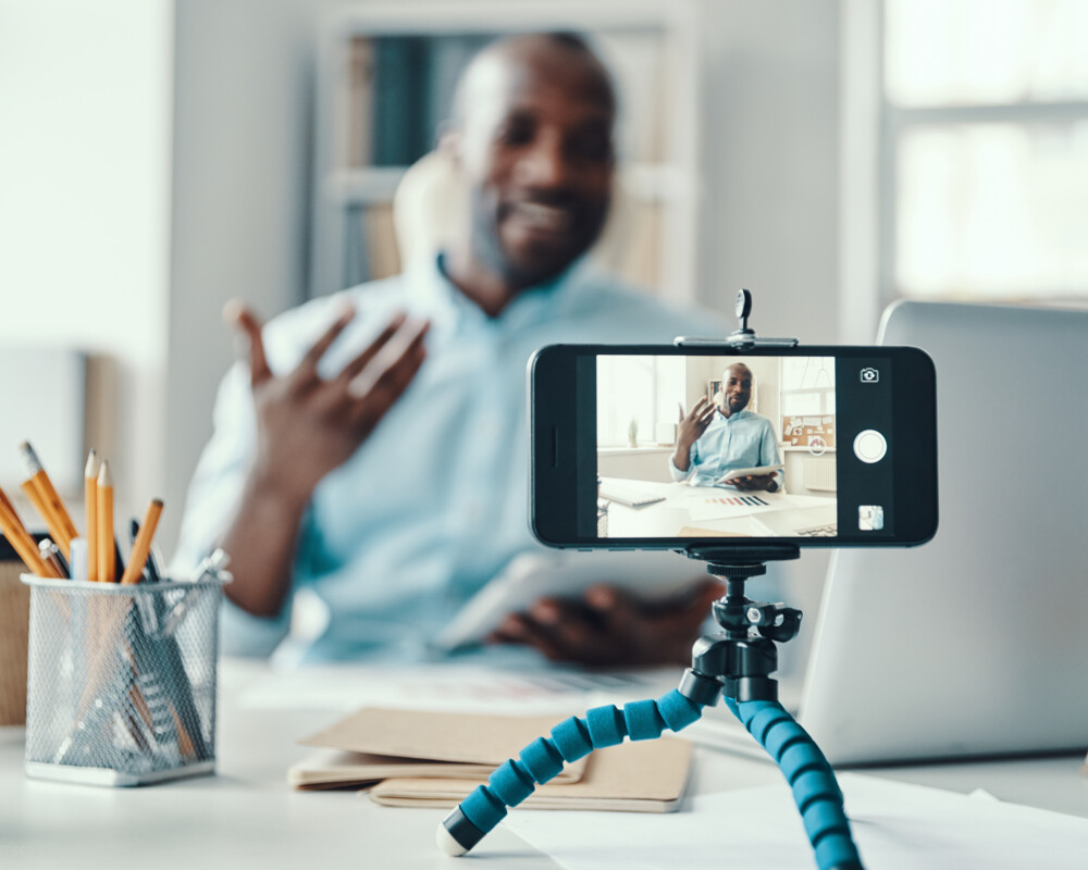 Influencer am Tisch sitzend, erstellt ein Video (Symbolbild)